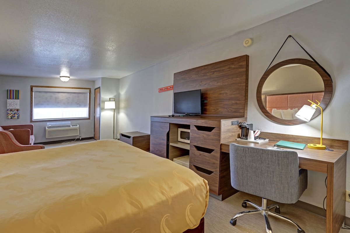 A hotel room with a bed, desk, chair, television, and a large mirror.