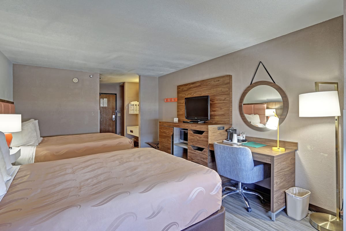 A hotel room with two beds, a desk with a computer, a TV, and a mirror.