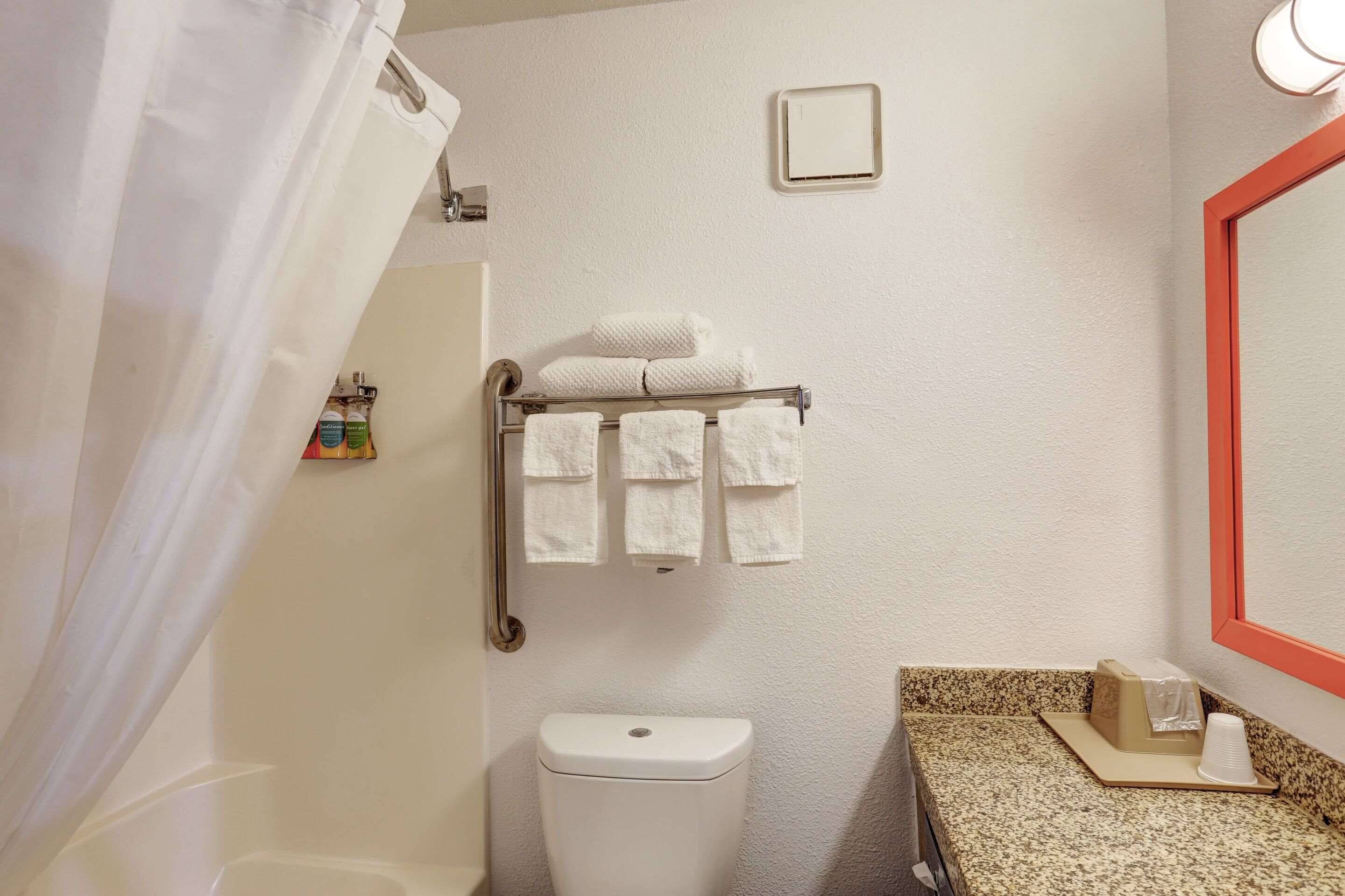 Un baño con inodoro, toallero con toallas, secamanos y espejo.