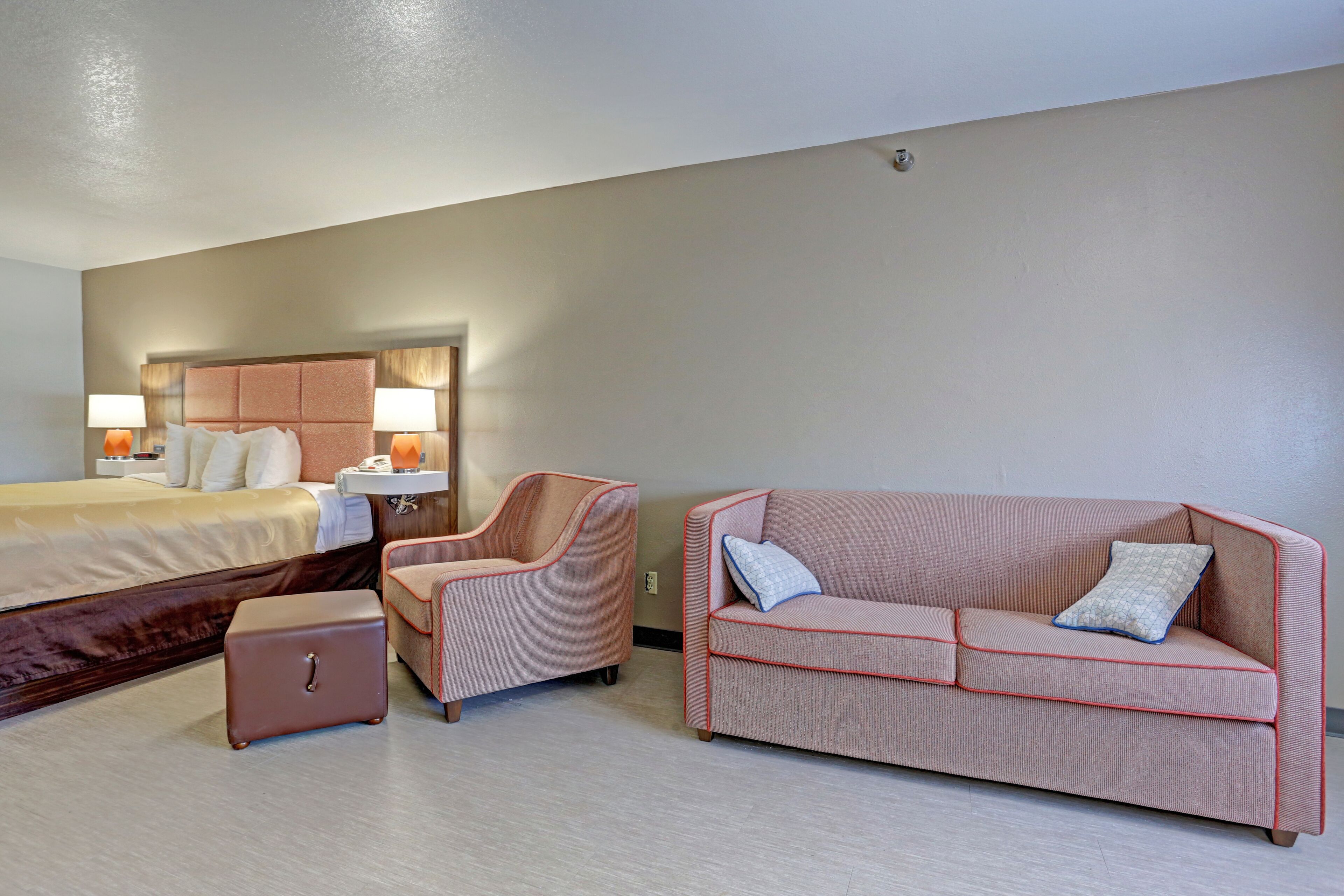 Una camera d'hotel con un letto, un divano rosa, una poltrona e un tavolino.