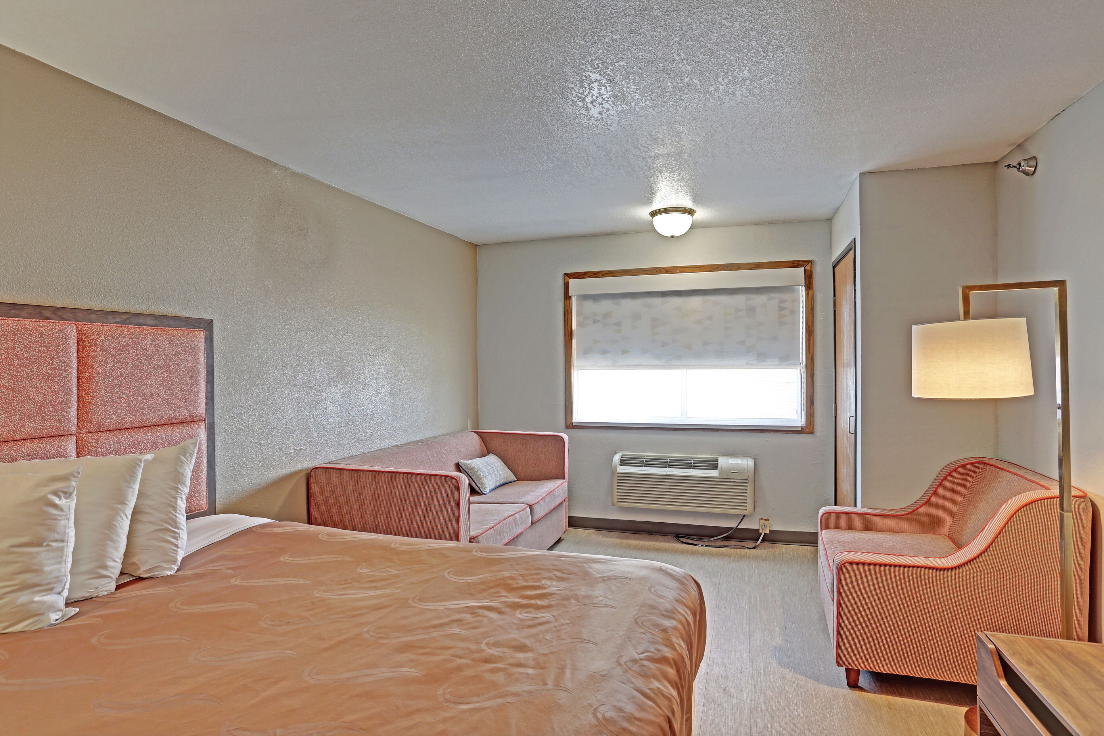 A hotel room with a large bed, two sofas, a desk, and a window with blinds.