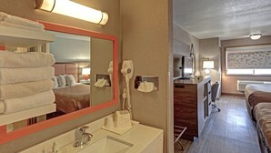 A hotel room with a large mirror, a sink, a hairdryer, a desk with a chair, and a bed. - Quality Inn Pierre - Fort Pierre (Pierre)