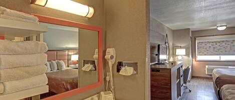 Habitación de hotel con un espejo grande, un lavamanos, un secador de pelo, un escritorio con una silla y una cama.