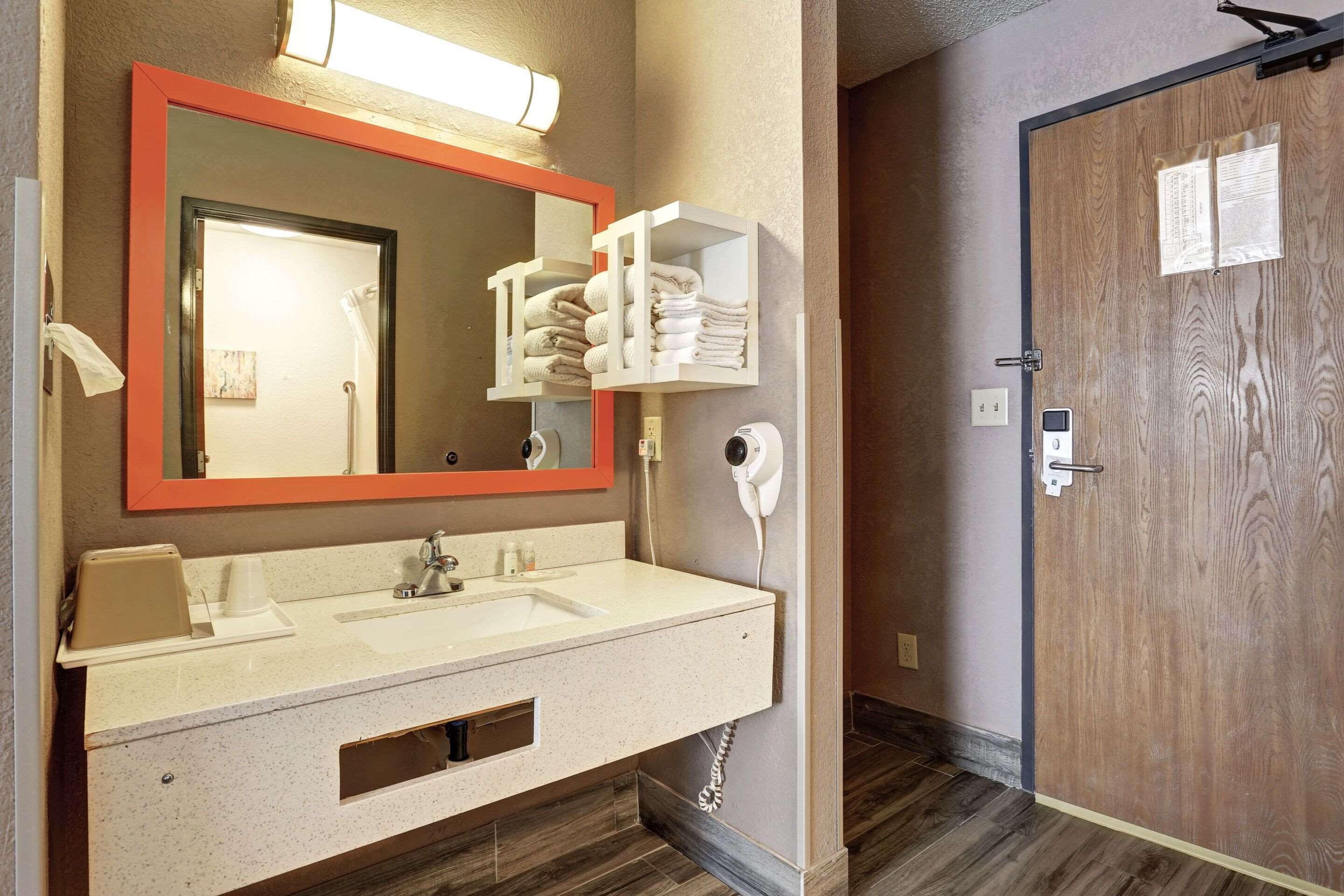 Un baño con lavamanos doble, un espejo con marco anaranjado, un perchero y una puerta con panel de madera.