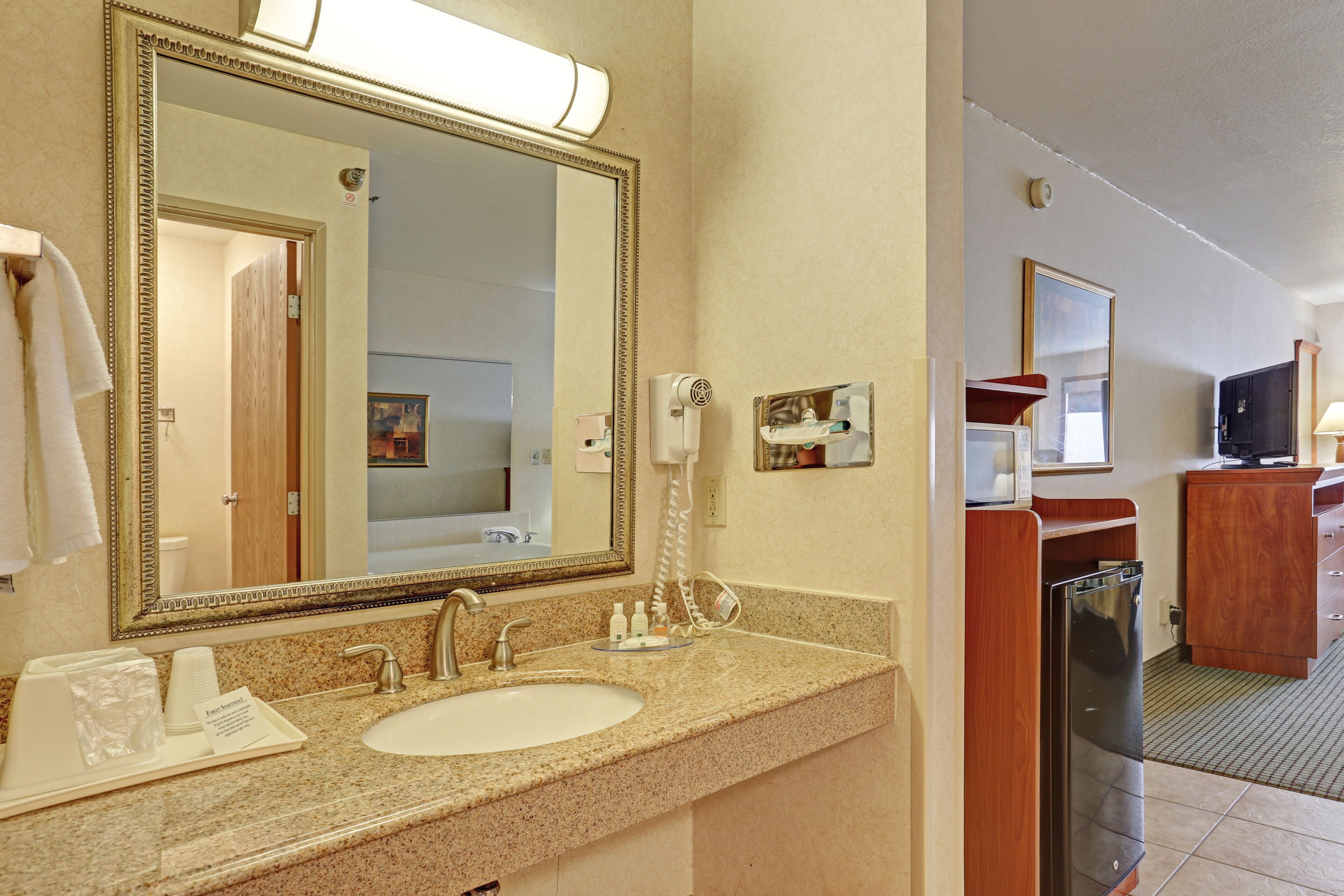 Un baño de hotel con un espejo grande, lavamanos y refrigerador.