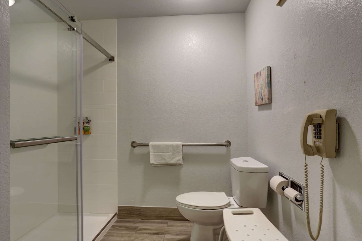 A bathroom with a glass shower enclosure, a toilet, a bidet, and a telephone mounted on the wall.