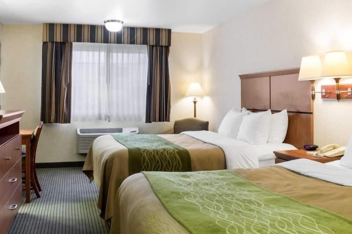 A hotel room with two beds, a desk, a chair, a window with curtains, a lamp, and a telephone.