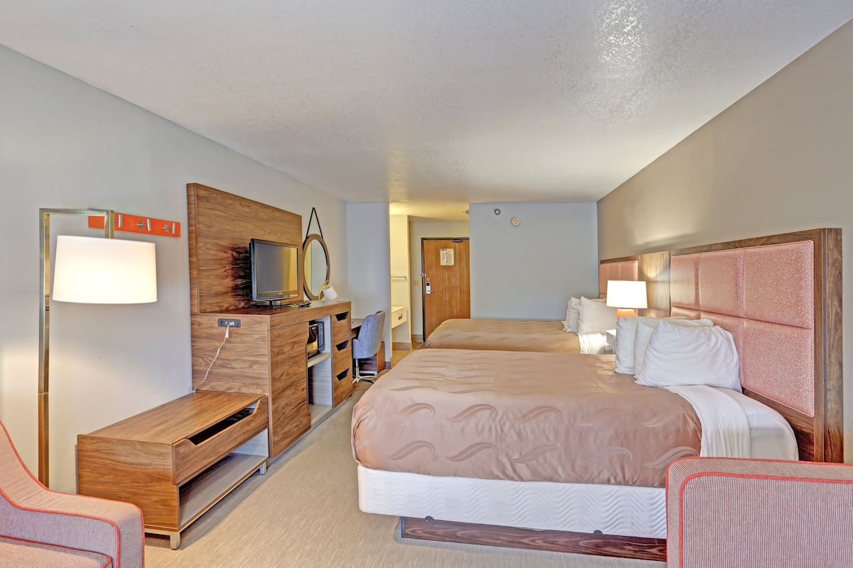 A hotel room with a bed, a desk with a computer, a chair, a TV, and a lamp.