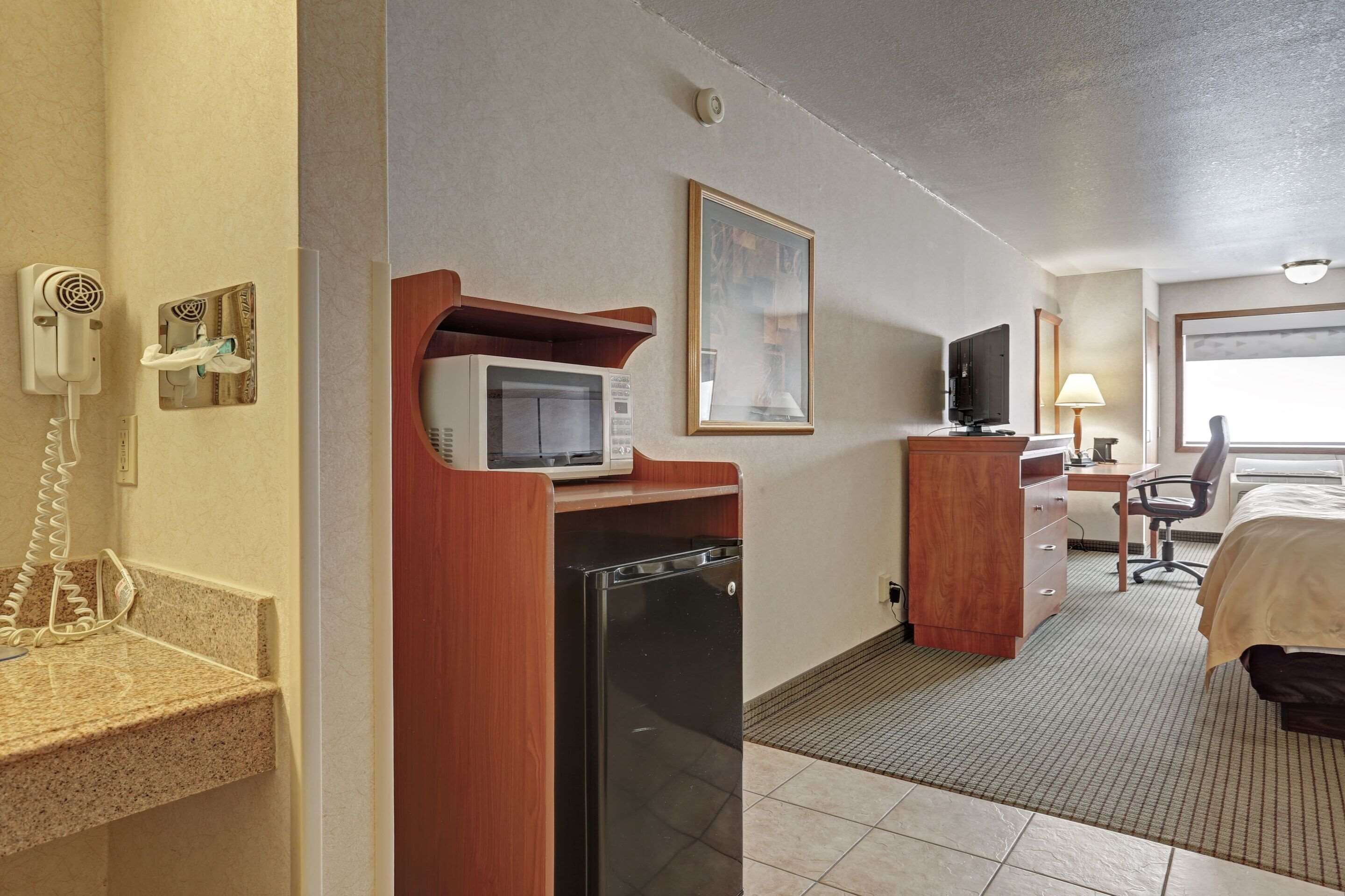 Ein Hotelzimmer mit Mikrowelle, kleinem Kühlschrank, Schreibtisch mit Stuhl, Bett und Fernseher.