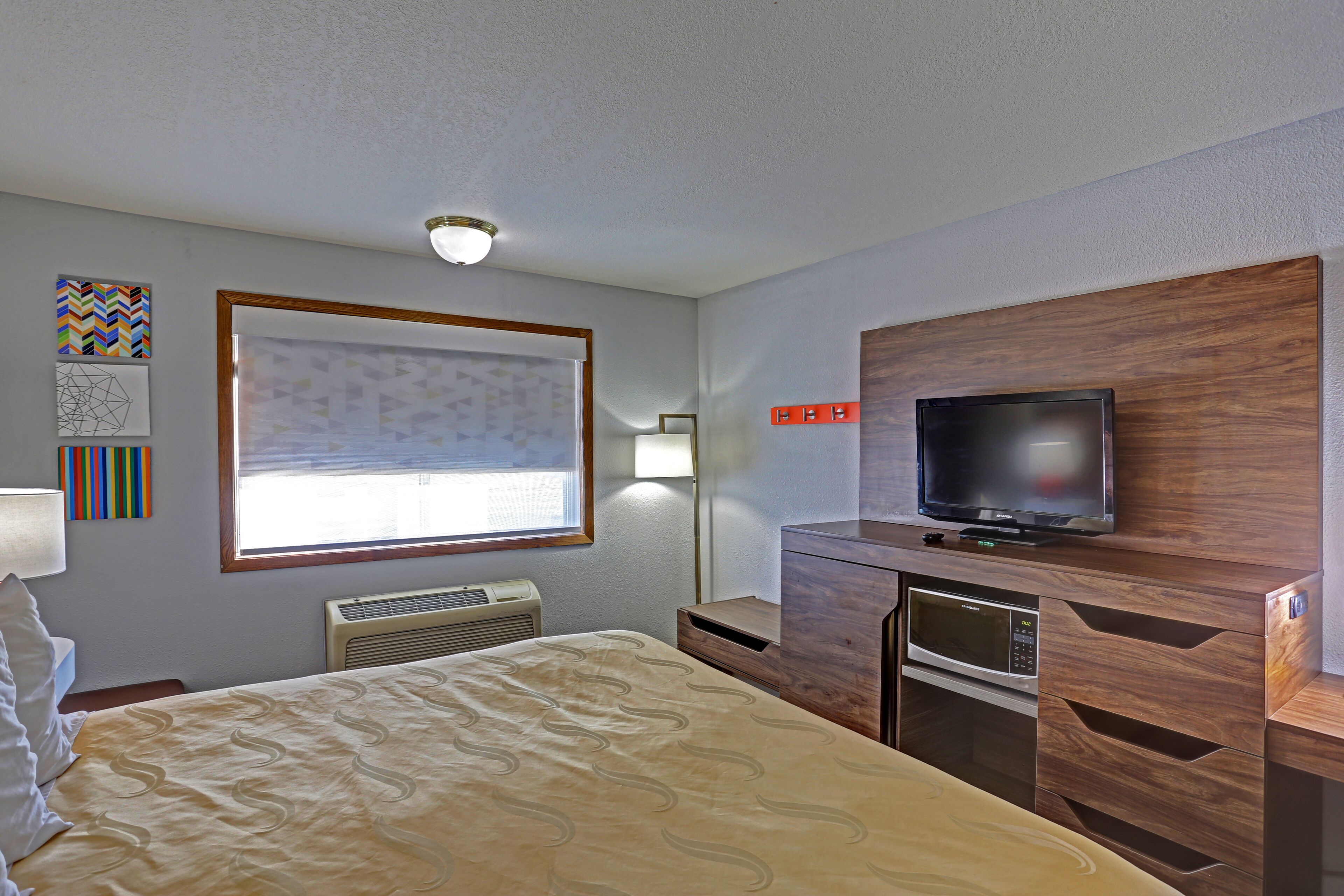 A hotel room with a bed, a TV mounted on a wooden cabinet, a microwave, and a heater.