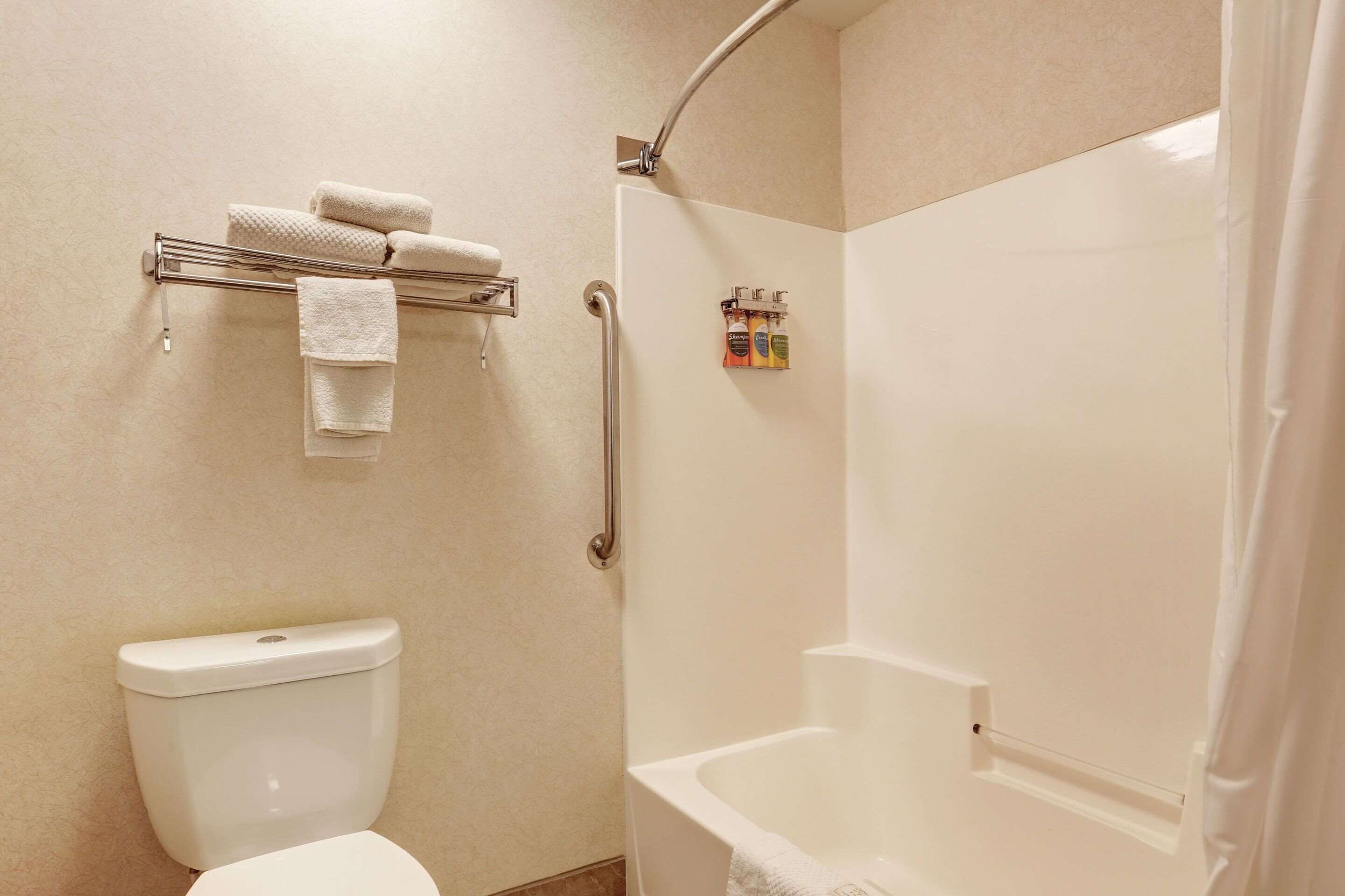 Une salle de bain comprenant des toilettes, un porte-serviettes avec des serviettes, une douche équipée d’une barre d’appui et un flacon de shampoing.