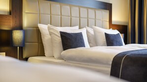 A neatly made bed with white and dark pillows, a wooden headboard, and a bedside lamp.