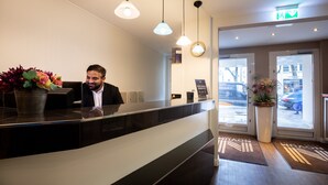 A reception desk with a man seated behind it, a potted plant, and a sign indicating an exclusive membership.