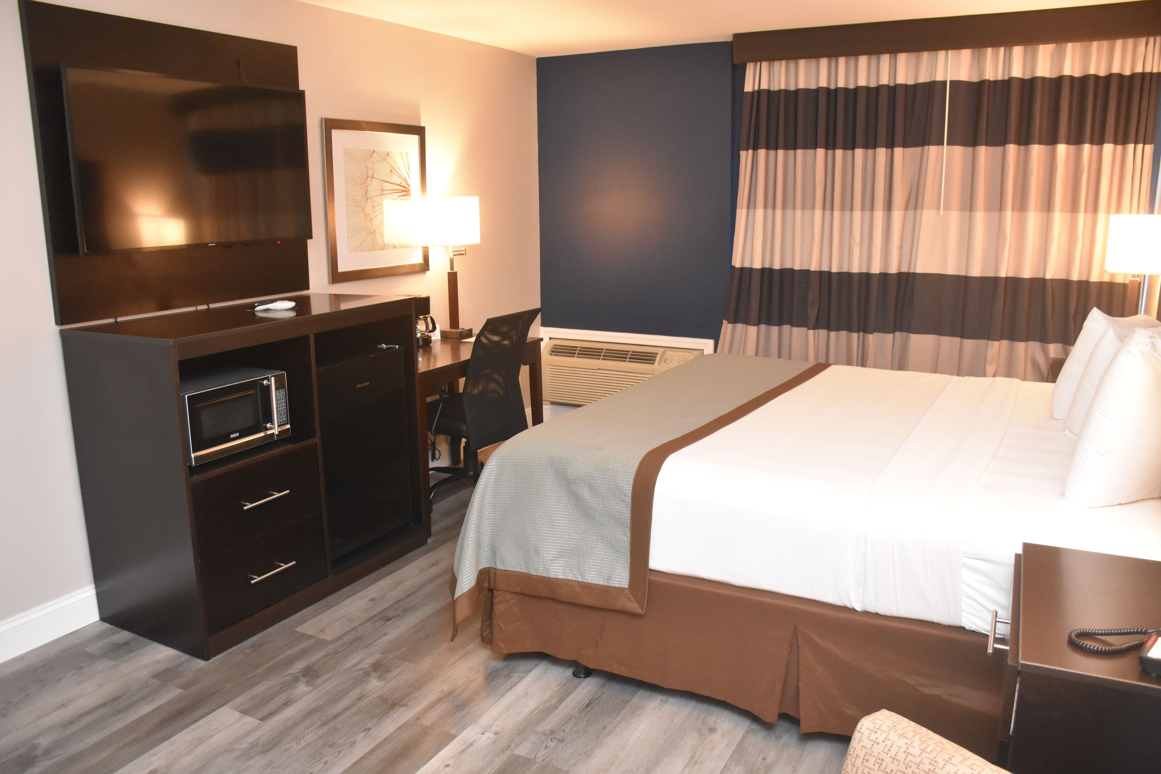 Habitación de hotel con una cama grande, un escritorio con una silla, un televisor de pantalla plana, un microondas y una ventana con cortinas a rayas.