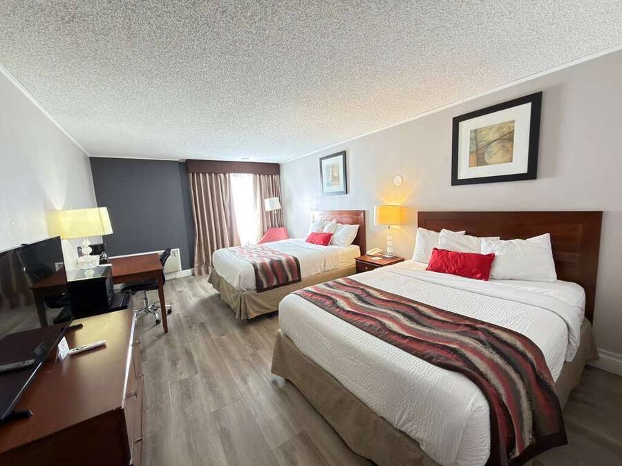 Habitación de hotel con dos camas, un escritorio, una silla, un televisor y una lámpara.