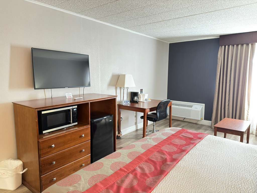A hotel room with a bed, a desk, a television, a microwave, a chair, and a window with curtains.