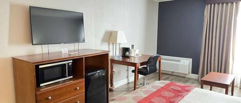 A hotel room with a bed, a desk, a television, a microwave, a chair, and a window with curtains.