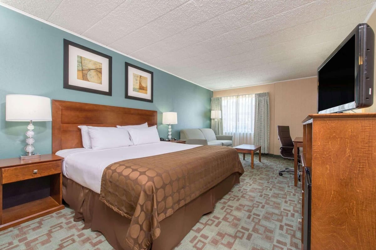 A hotel room with a large bed, two bedside tables, a desk, a chair, a television, and two framed pictures on the wall.