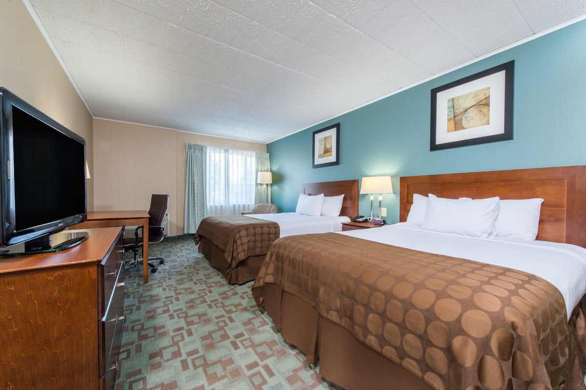 A hotel room with two beds, a desk with a TV, a chair, and a desk lamp.