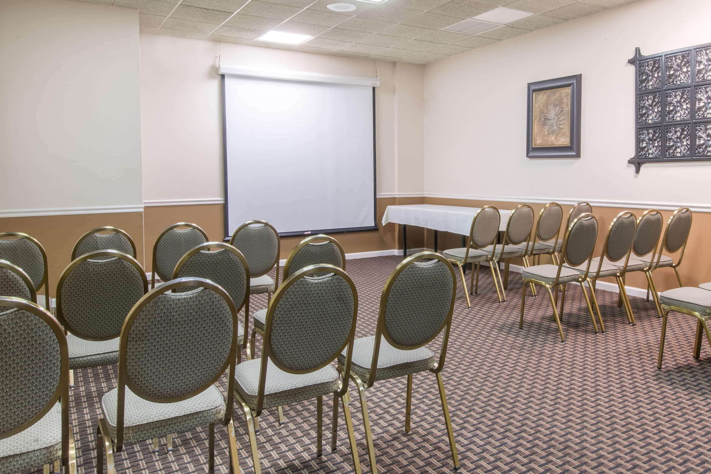 A conference room with rows of chairs, a projector screen, and a table.