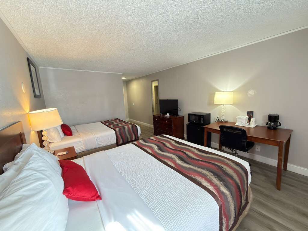 Habitación de hotel con dos camas, un escritorio, una silla, un televisor y una cafetera.