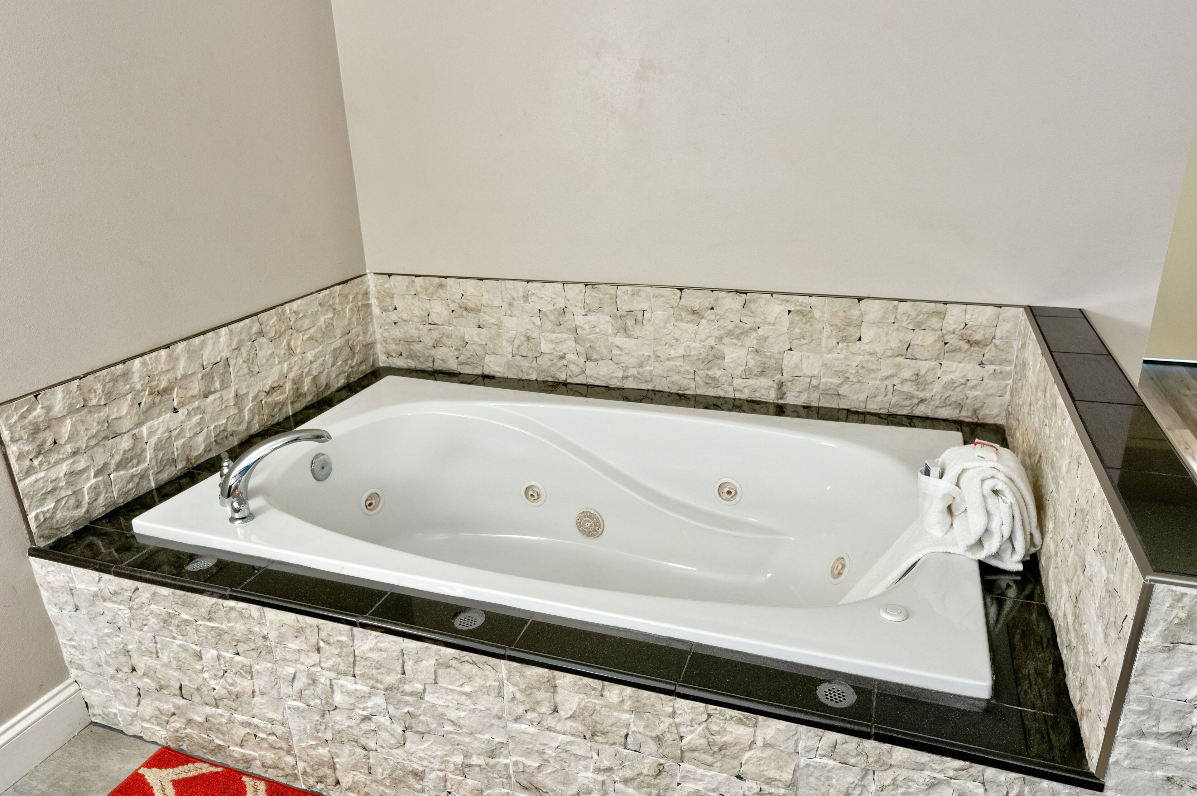 A rectangular bathtub with a black countertop and stone wall surrounds.