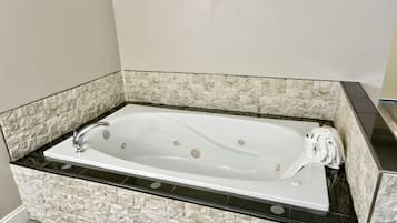 A rectangular bathtub with a black countertop and stone wall surrounds.