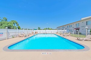 Piscina rectangular con borde de azulejos, rodeada de sillas de descanso y una valla.