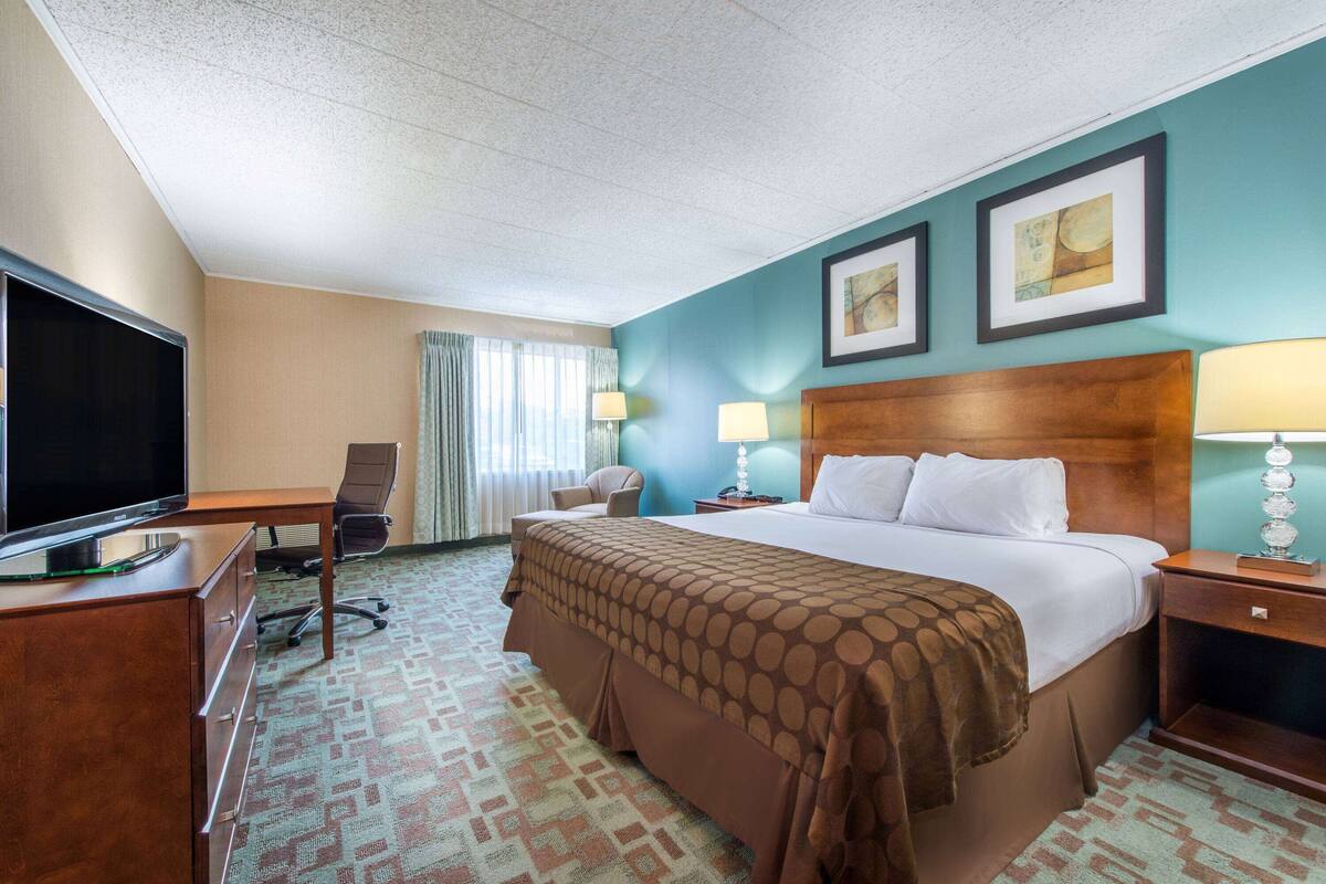A hotel room with a large bed, a desk with a TV, a chair, and two bedside lamps.