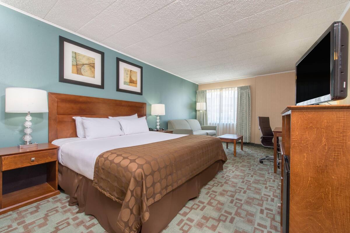 A hotel room with a large bed, two bedside tables with lamps, a desk with a chair, a television, and two framed pictures on the wall.