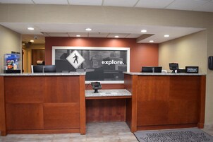 Un mostrador de recepción de hotel con un cartel grande que dice 'explore'. Hay dos mostradores de recepción, una máquina expendedora y un cartel de 'Hilton Honors'.