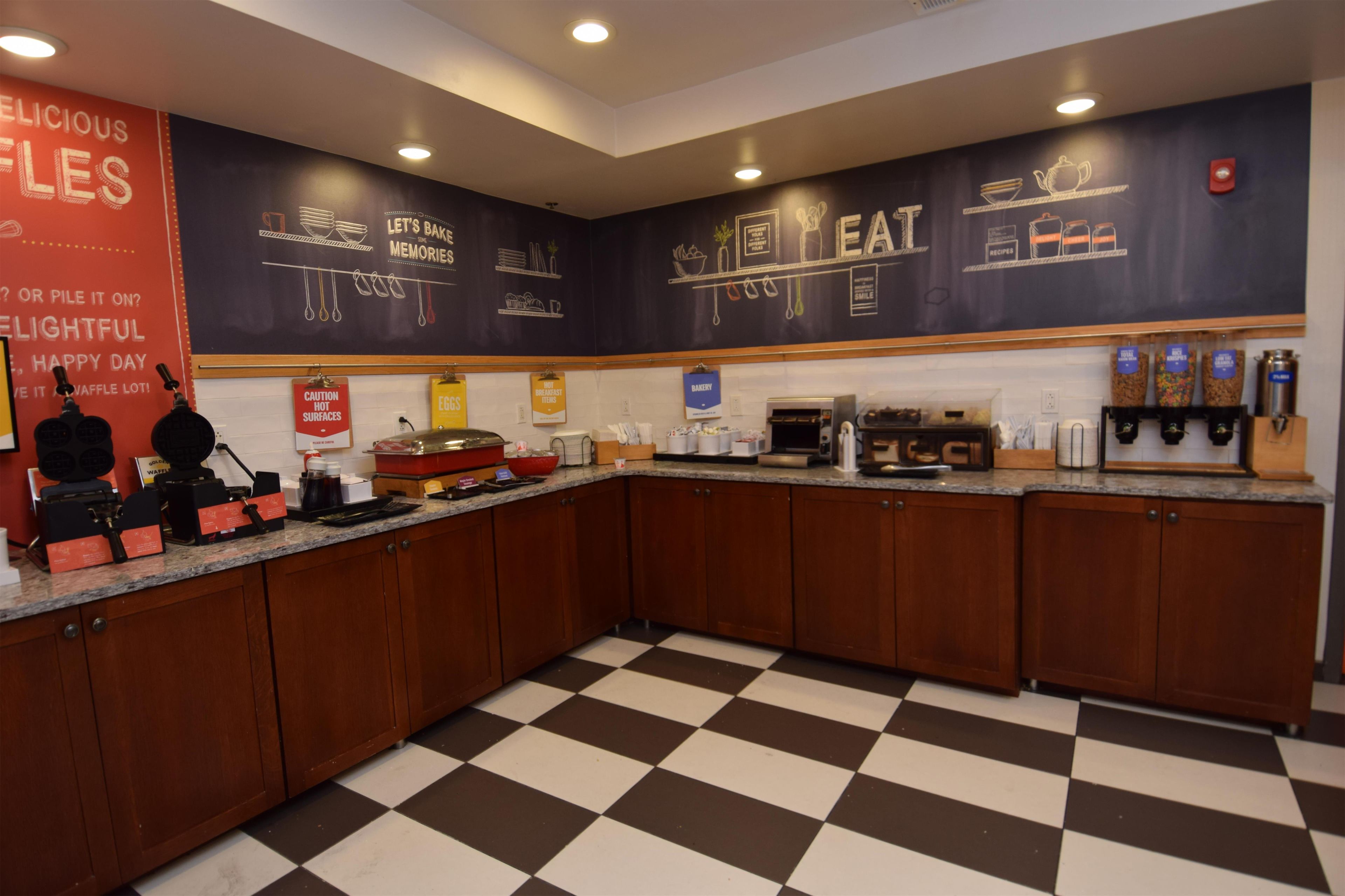 A kitchen with a checkered floor, wooden cabinets, and various appliances including a coffee machine and waffle maker.