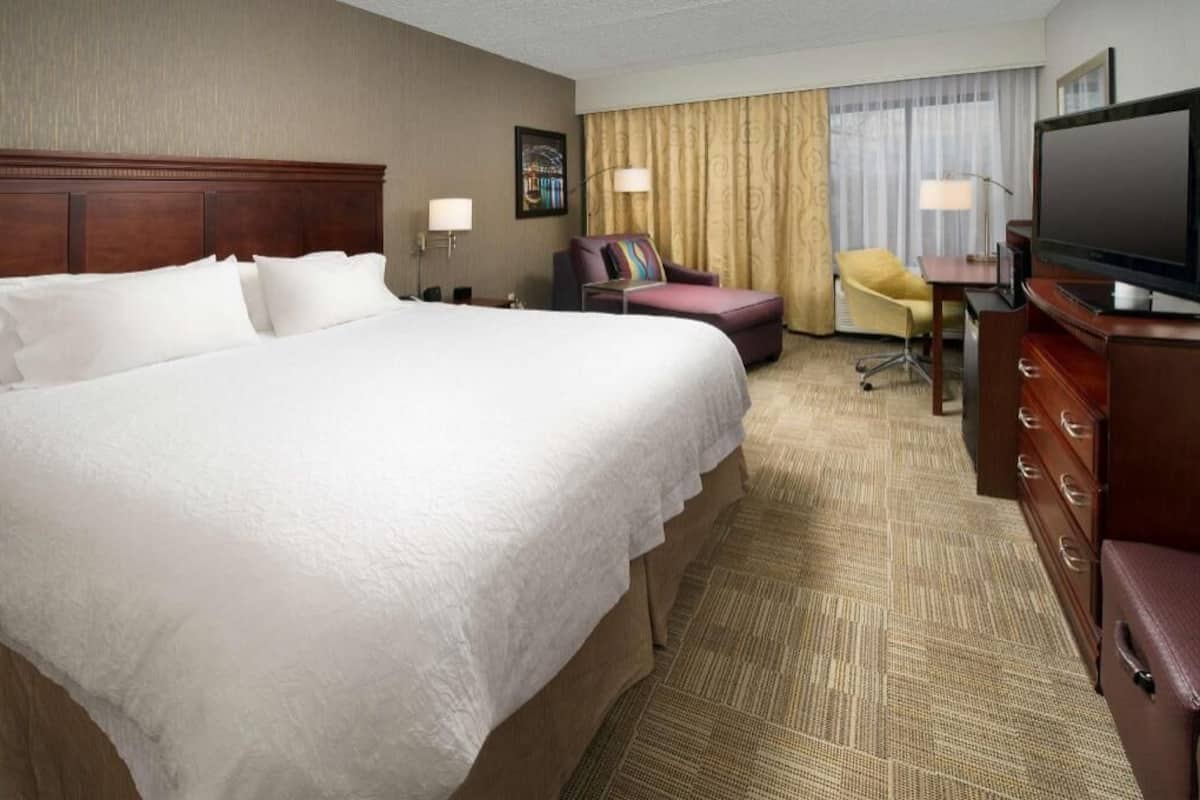 A hotel room with a large bed, a desk with a flat-screen TV, a chair, and a sofa.