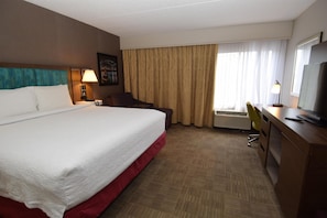 A hotel room with a large bed, a desk with a chair, a television, and a window with curtains.