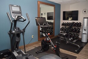 Une salle de sport équipée d’appareils de cardio, d’haltères et d’un téléviseur fixé au mur.
