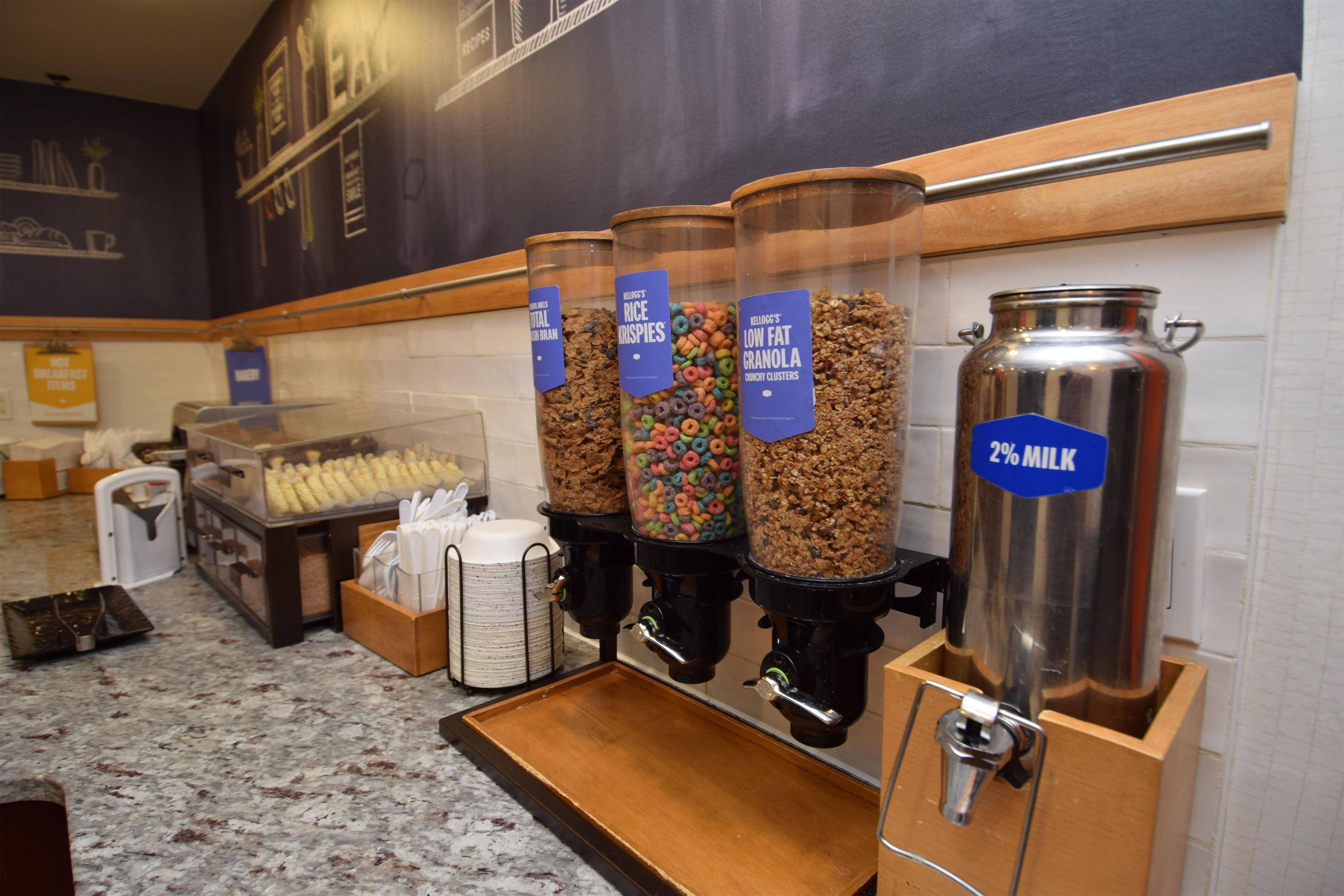 A breakfast buffet with various cereal options and a milk dispenser.