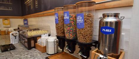 A breakfast buffet with various cereal options and a milk dispenser.