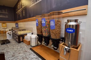 Un bufé de desayuno con varias opciones de cereales y un dispensador de leche.