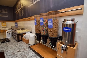 A breakfast buffet with various cereal options and a milk dispenser.
