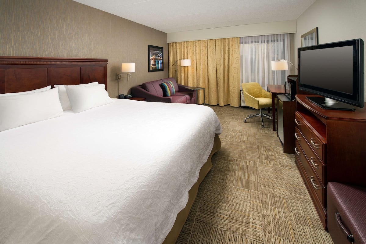 A hotel room with a large bed, a television, a desk with a chair, and a window with curtains.