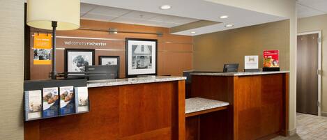 A reception desk with a wooden finish, a large lamp, framed pictures, and informational posters.