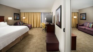 Ein Hotelzimmer mit einem großen Bett, einem Schreibtisch mit Computer, einer Couch und einem Fernseher.
