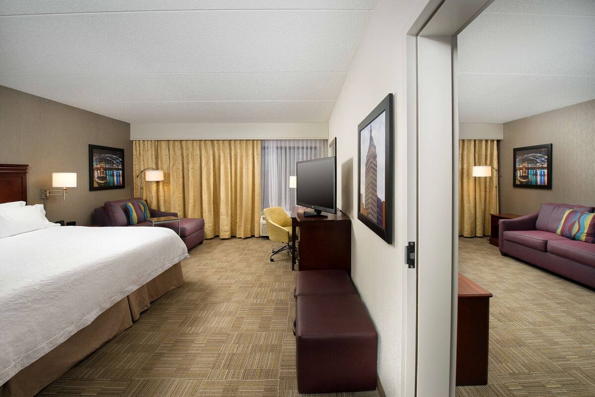 A hotel room with a large bed, a desk with a computer, a sofa, and a TV.