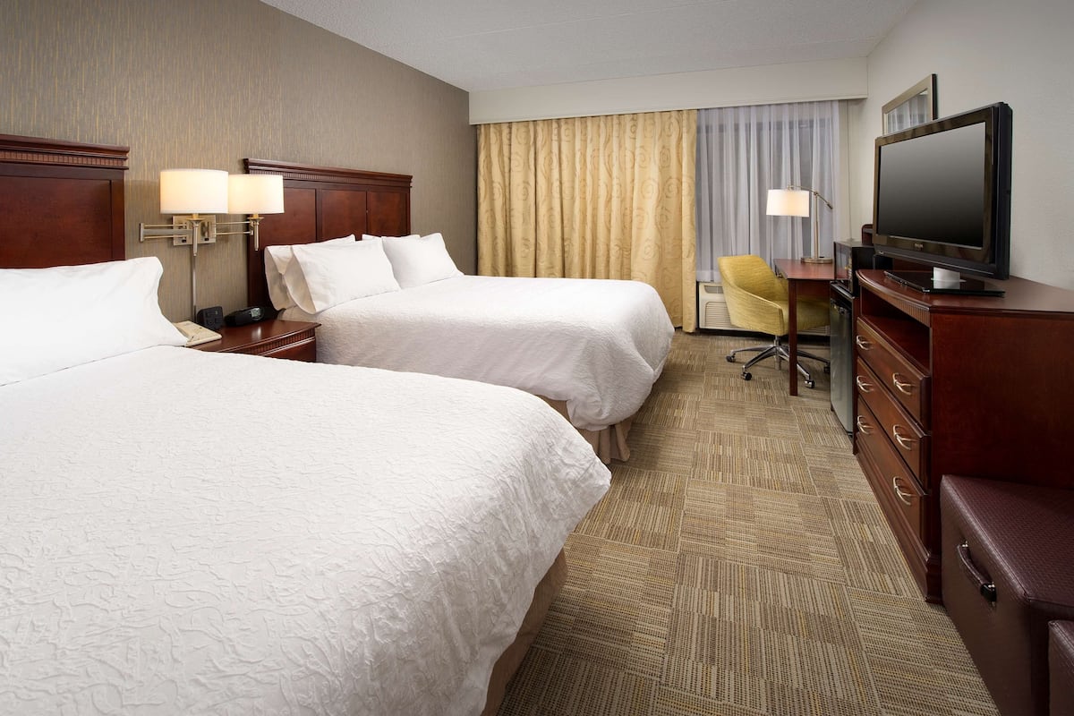 A hotel room with two beds, a television, a desk with a lamp, and a chair.