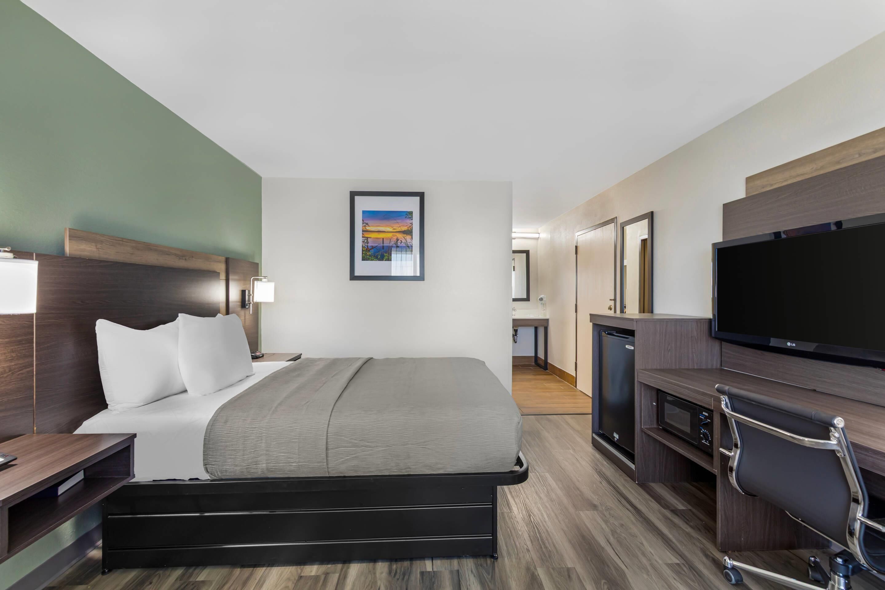 Habitación de hotel con cama, escritorio, televisor, microondas y baño al fondo.