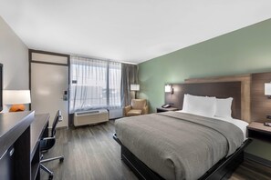A hotel room with a bed, desk, chair, and a large window with curtains.
