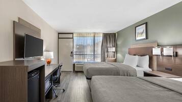 Habitación de hotel con escritorio, televisión, dos camas, ventana con cortinas e imagen enmarcada en la pared.