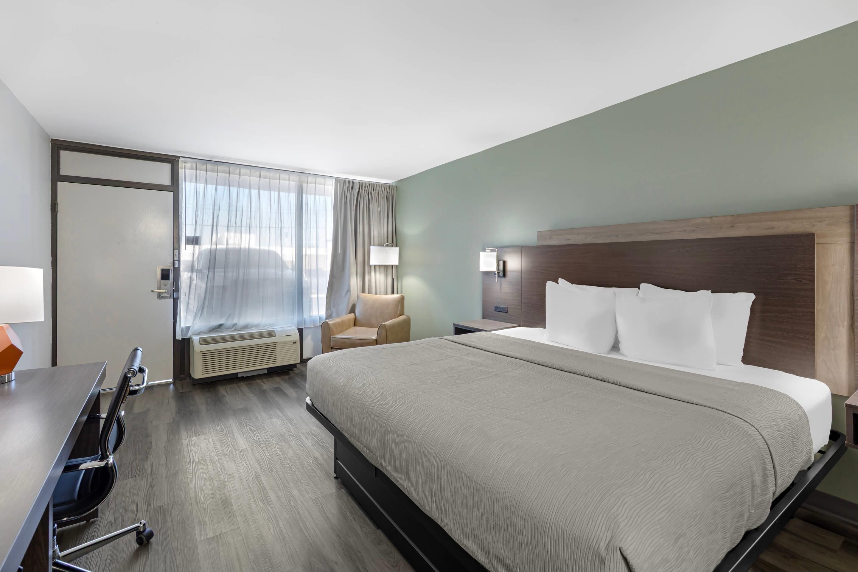 Een hotelkamer met een bed, een bureau, een stoel, een lamp en een raam met gordijnen.