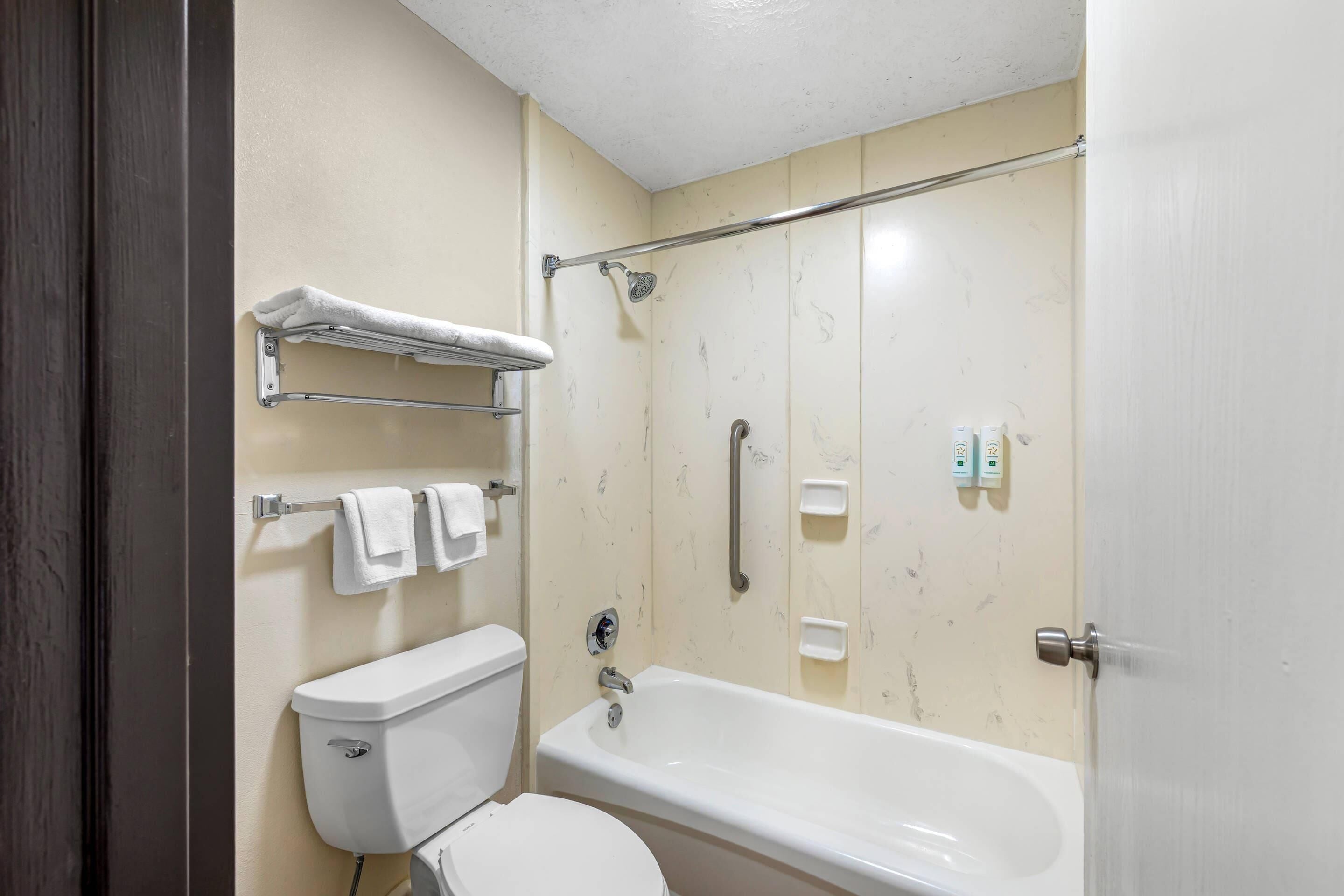 Un baño con inodoro, bañera, toallero y barra para cortina de ducha.