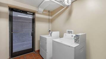 A laundry room with two white washers and dryers, a tiled floor, and a door with a metal handle.